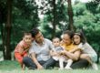Mother, father, and three kids sitting close together on grass