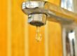 Close up of water dripping out of a faucet with a yellow background