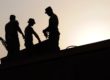 backlit outline of 3 workers on a roof