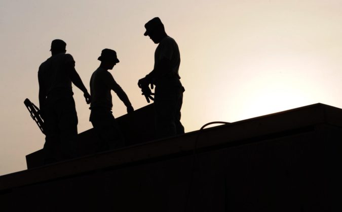 backlit outline of 3 workers on a roof