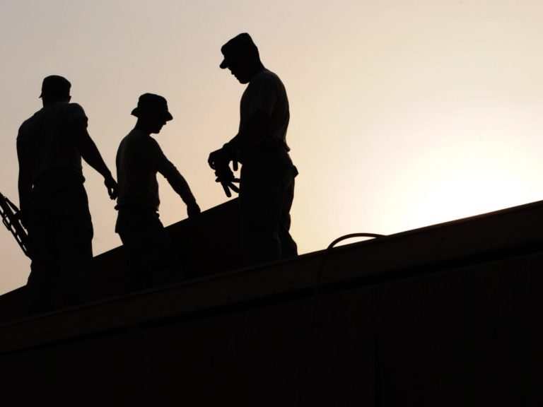 backlit outline of 3 workers on a roof