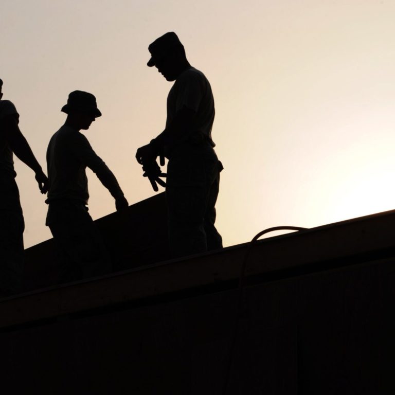 backlit outline of 3 workers on a roof