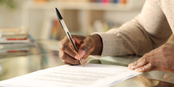 Close up of black man hands signing document on a desk at home